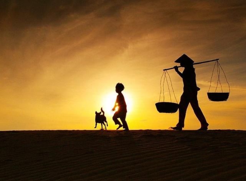 Người mẹ gánh quang gánh, dẫn con và chó đi dưới hoàng hôn