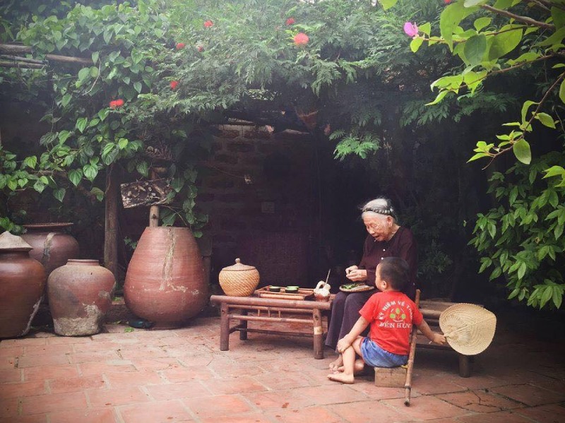 Bà ngồi ngoài hiên trò chuyện cùng cháu nhỏ trong khung cảnh quê
