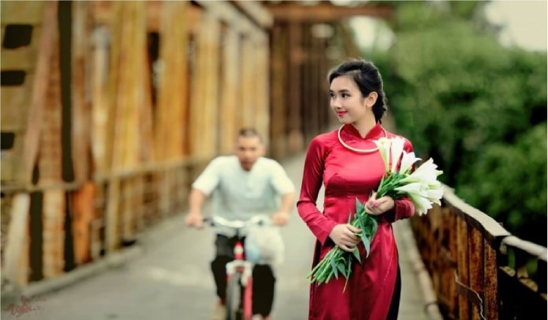 Thiếu nữ áo dài đỏ cầm hoa loa kèn trên cầu
