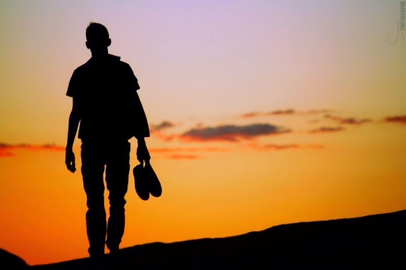 Bóng người đàn ông cầm giày đi một mình dưới hoàng hôn
