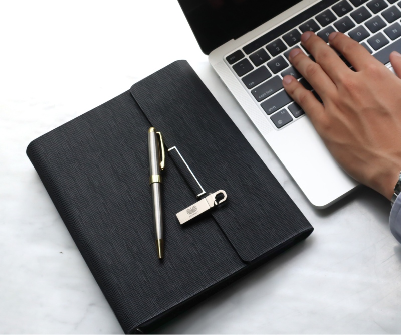 sổ tay bìa đen kèm bút đặt bên laptop